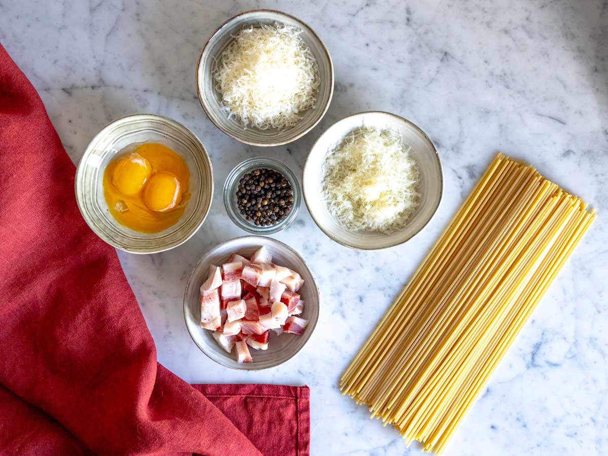 Egg yolks, diced guanciale, spaghetti, black pepper, and grated cheeses.