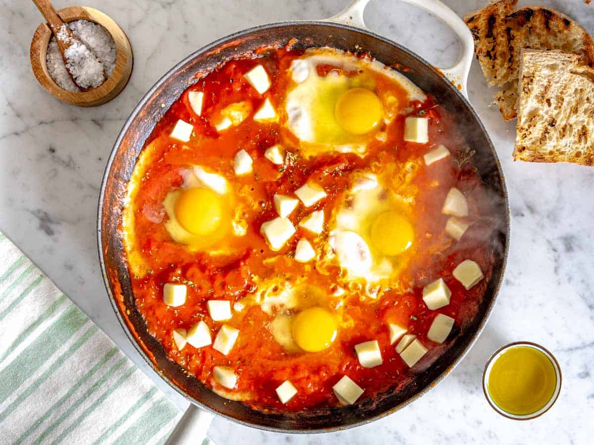 four eggs and cheese with marinara sauce in a skillet