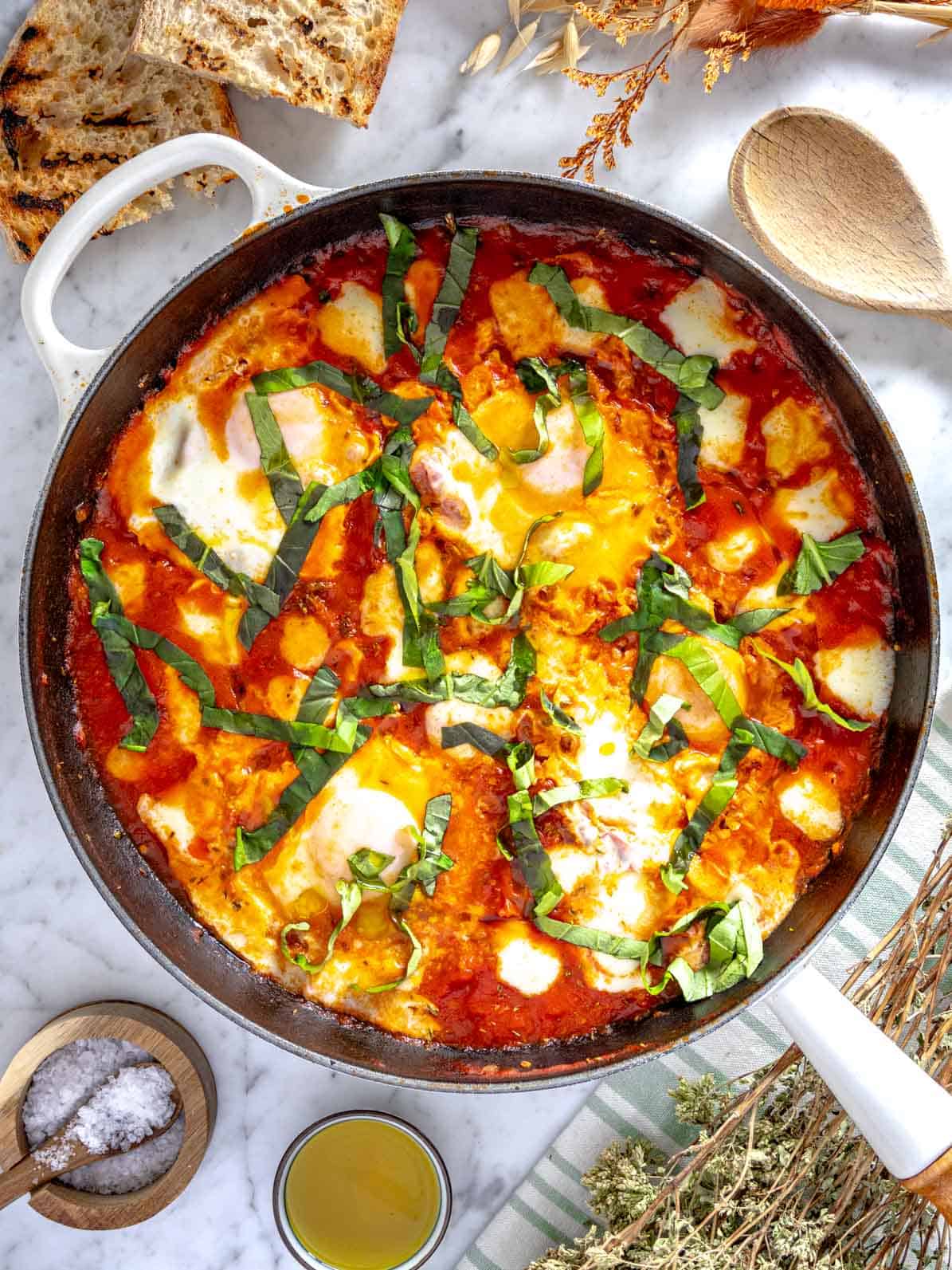 Eggs in purgatory in a white skillet with fresh basil and bread