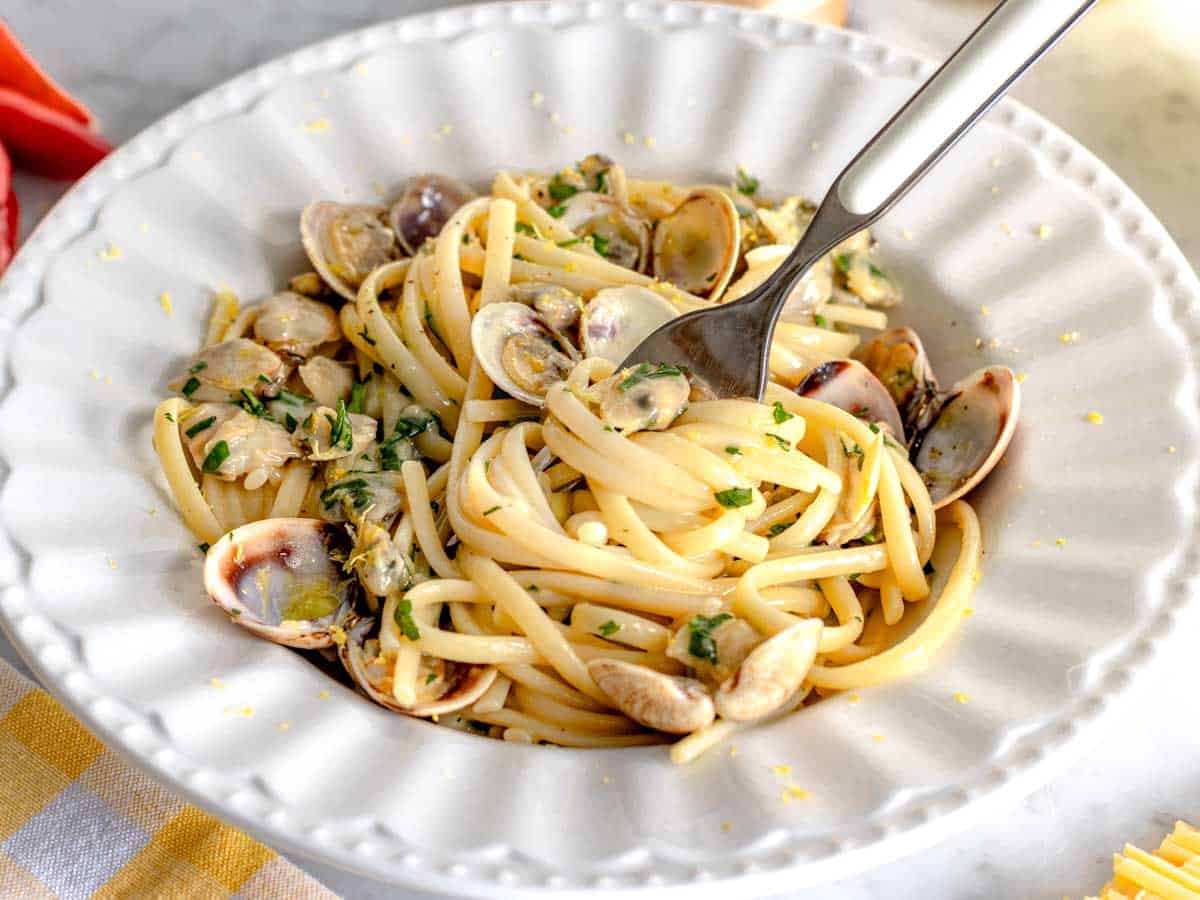 Linguine with clam sauce in a white bowl with a grating of lemon zest.