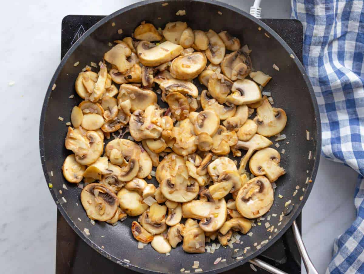 Step 3 onions and mushrooms softening in a hot pan.