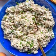 Bowl of tuna egg salad on the table with bread and simple lunch sides.