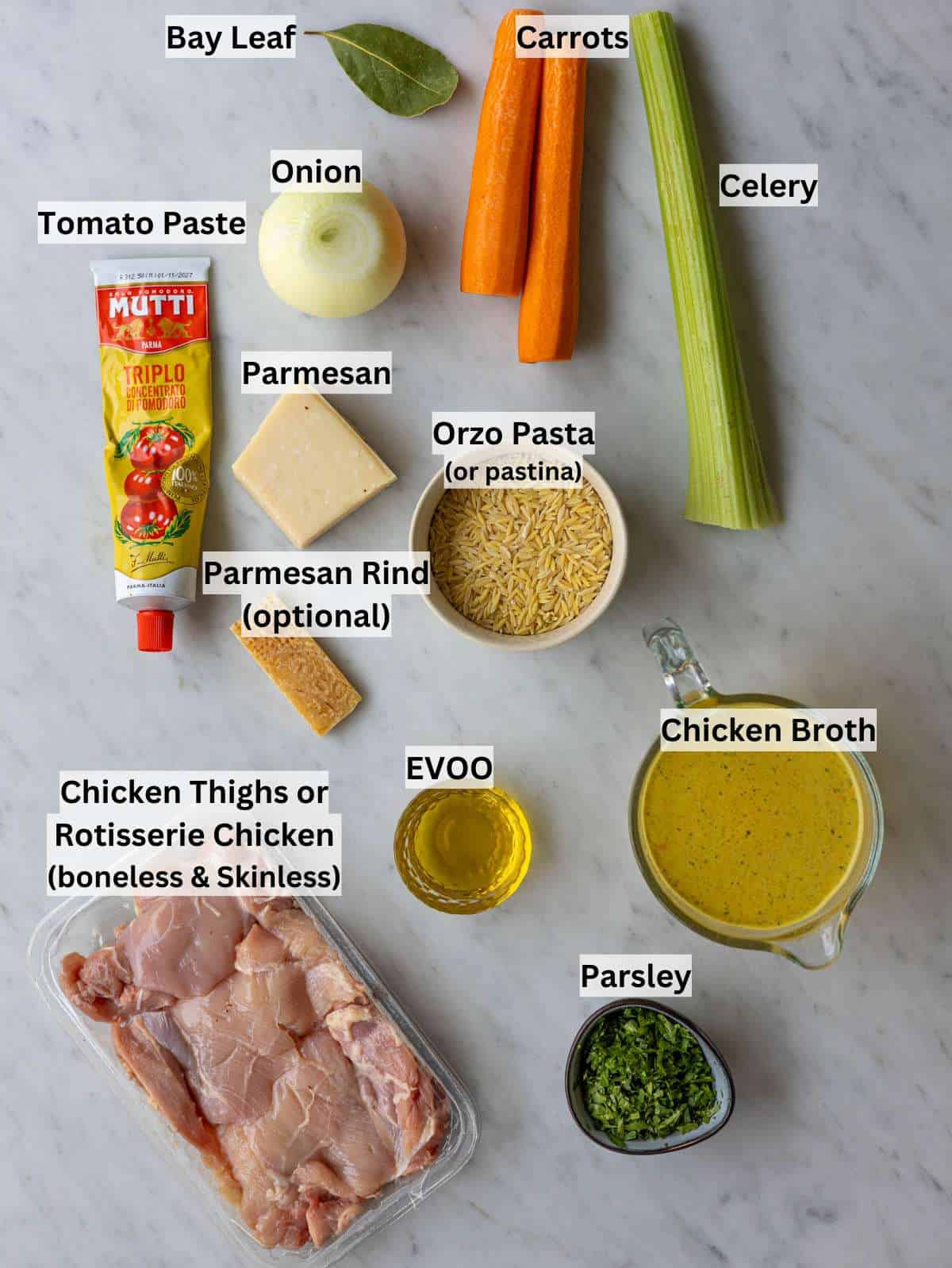 Chicken broth, raw chicken, orzo, vegetables, Parmesan, bay leaf, olive oil on a kitchen counter.