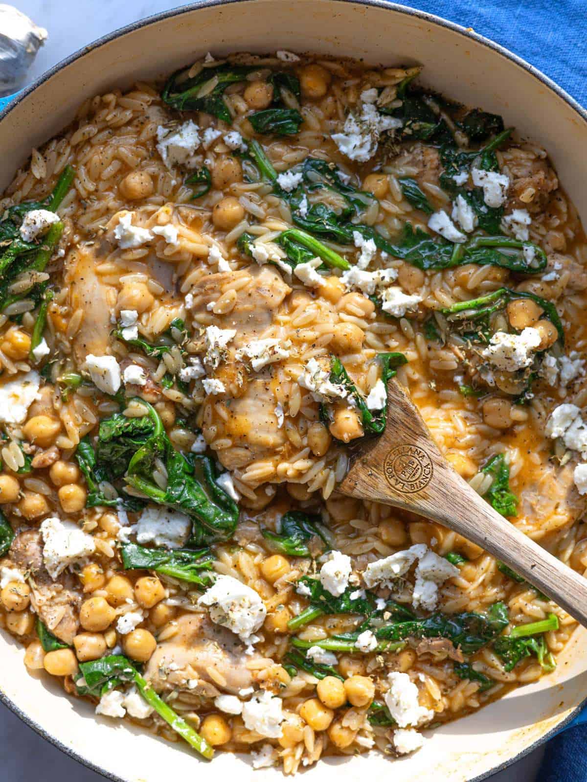 Finished lemon chicken orzo in a skillet with chicken thighs chickpeas spinach and feta.