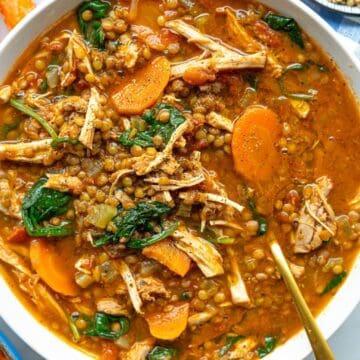 Hearty bowl of Mediterranean-style soup with chicken, lentils, and greens on a rustic table.
