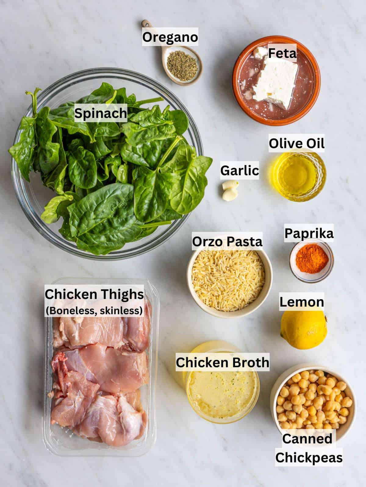 Ingredients for lemon chicken orzo arranged on a marble surface with fresh lemon and herbs.