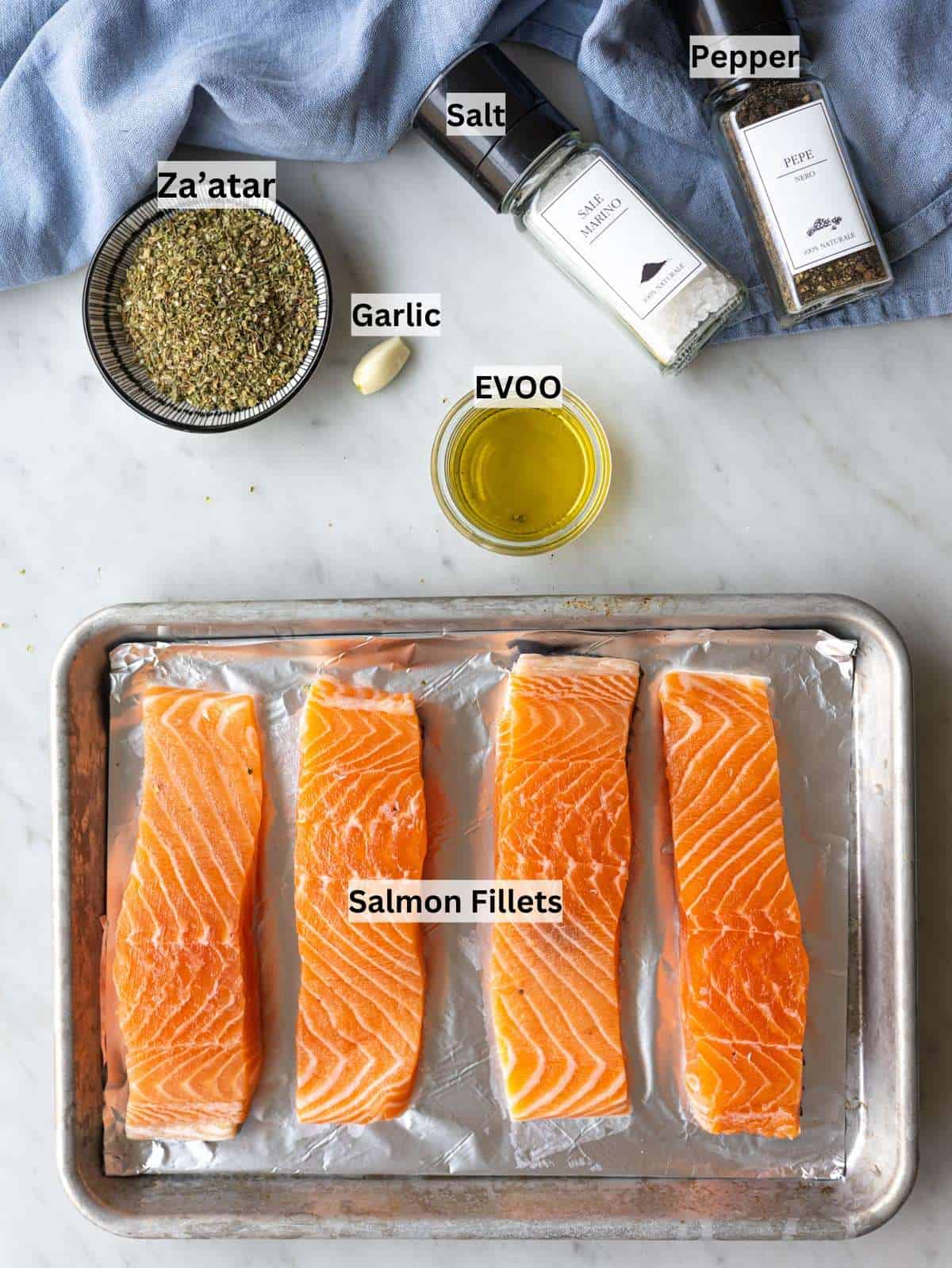 Raw salmon fillets, olive oil, garlic, salt, pepper, and za’atar arranged on a kitchen counter.