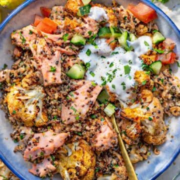 Sheet pan salmon quinoa bowl served in a bowl with quinoa, fresh vegetables, lemon, and creamy yogurt sauce.
