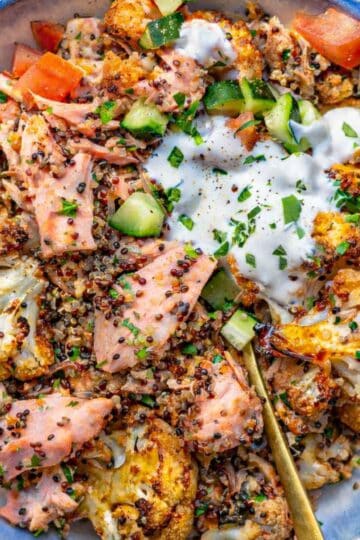 Sheet pan salmon quinoa bowl served in a bowl with quinoa, fresh vegetables, lemon, and creamy yogurt sauce.