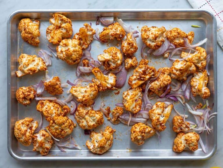 Step 2 Cauliflower and red onion spread on sheet pan, coated in spices, ready for roasting.