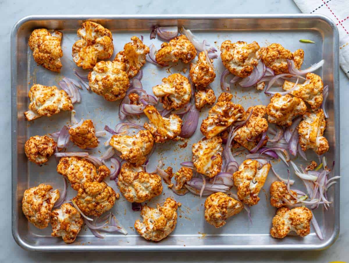 Step 2 Cauliflower and red onion spread on sheet pan, coated in spices, ready for roasting.