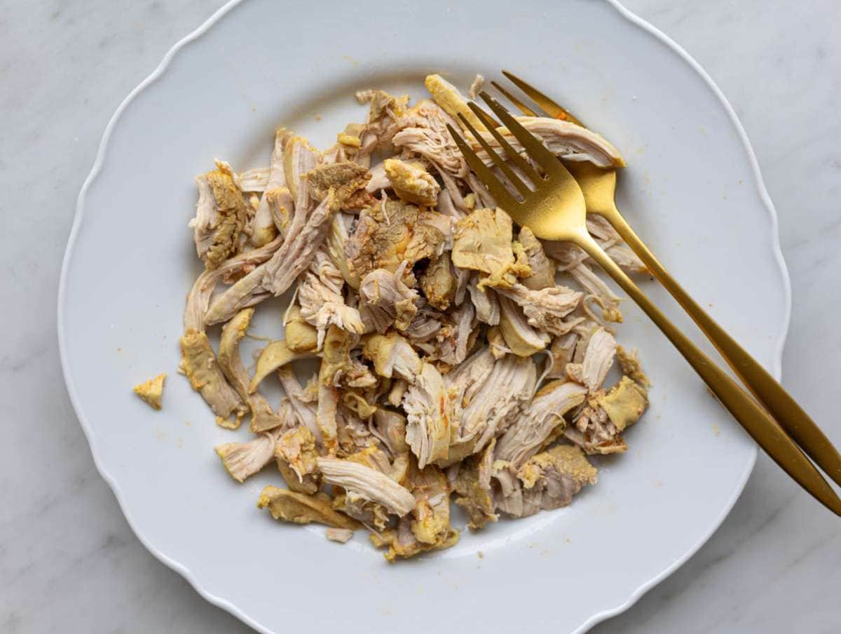 Step 3 Cooked chicken thighs being shredded with forks on a simple plate.