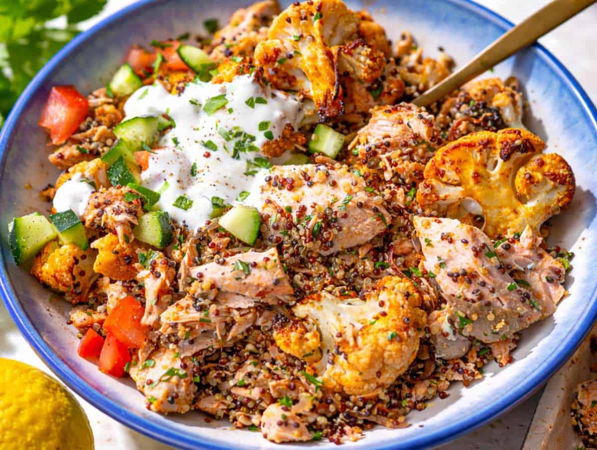 Step 5 Salmon quinoa bowl served with roasted cauliflower, flaked salmon, fresh cucumber, tomato, and creamy sauce.