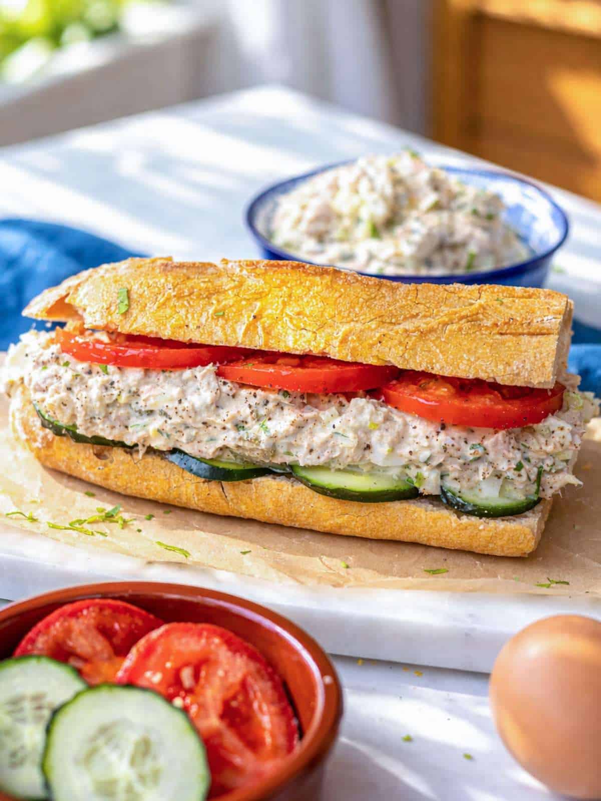 Tuna egg salad sandwich with crusty baguette, tomato, and cucumber.