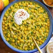 Bowl of turmeric chicken and rice with lemon wedges on side.