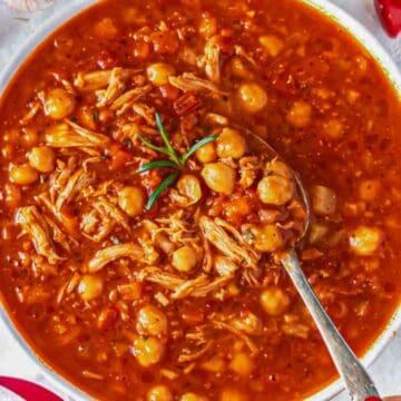 Close-up of spoonful showing tender chicken, chickpeas, and tomato-rich broth.