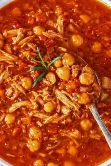 Close-up of spoonful showing tender chicken, chickpeas, and tomato-rich broth.