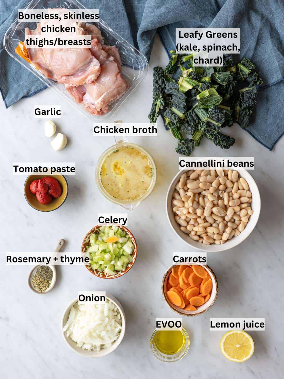 Raw chicken, white beans, kale, carrots, celery, onion, garlic, broth, and olive oil on a counter.