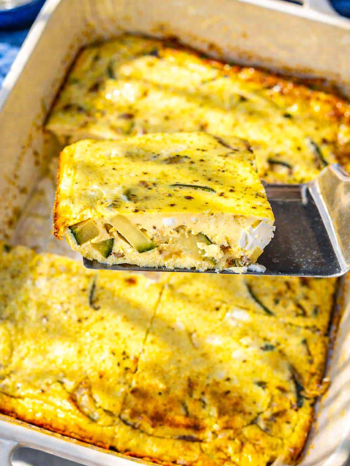 A detailed view of a creamy frittata slice showing melted feta and tender zucchini on marble.