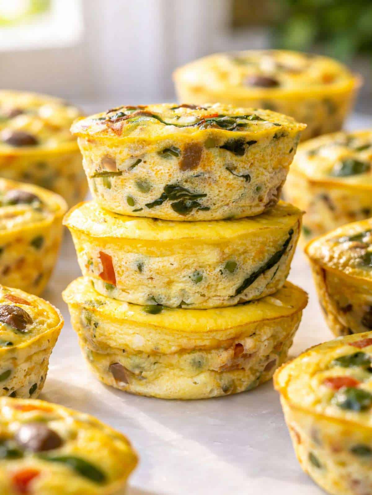 A dozen golden egg muffins with visible green spinach and red peppers on marble.