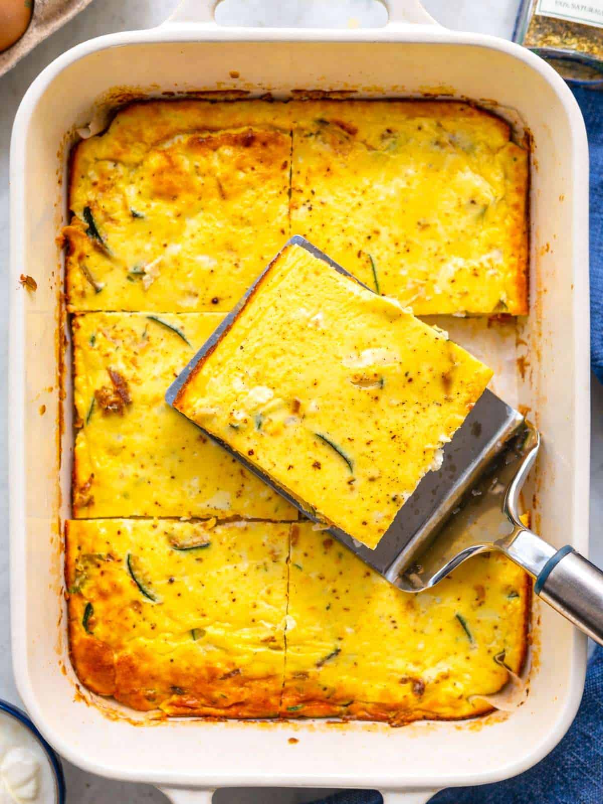 A golden baked frittata in a parchment-lined dish resting on a sunlit marble table.
