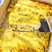 A sliced Greek yogurt frittata lifted on a spatula near a bright, airy window.