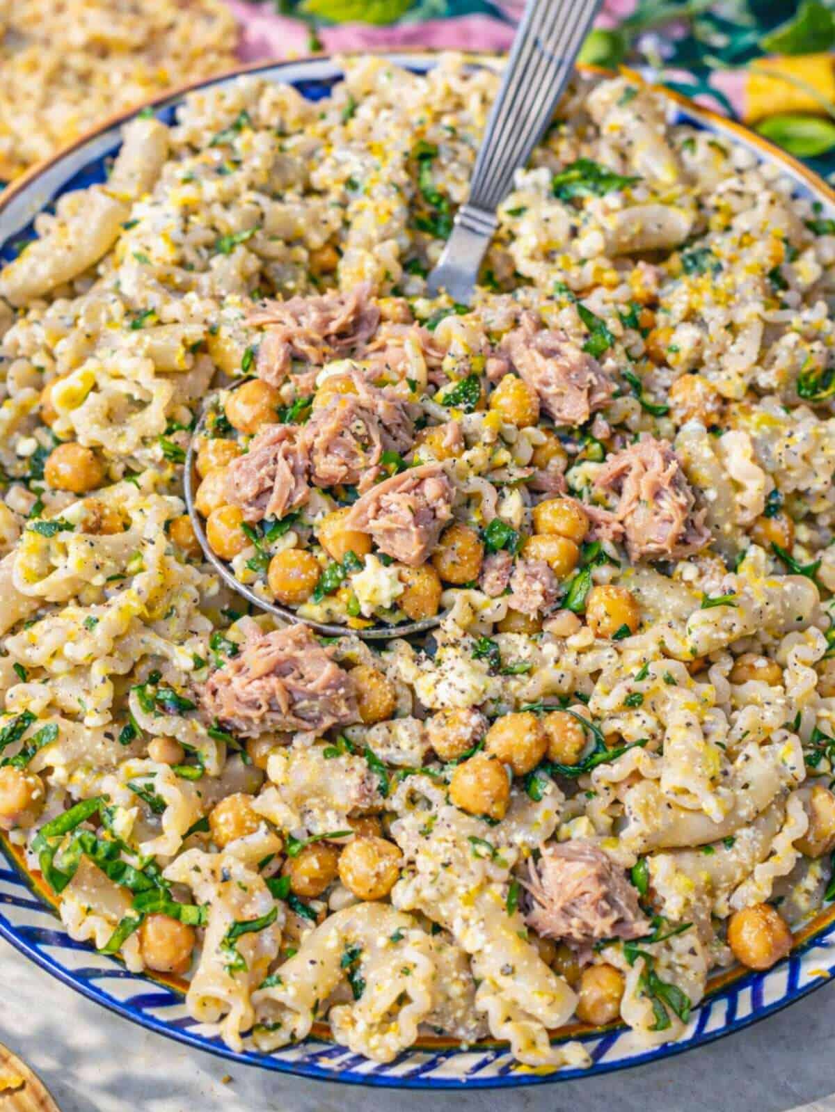 Close-up of lemon tuna pasta salad showing flaky tuna, glossy pasta, and herbs.