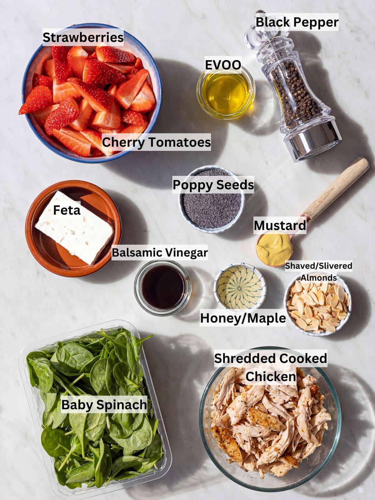 Fresh spinach, strawberries, cooked chicken, feta, almonds, and dressing ingredients on marble surface.
