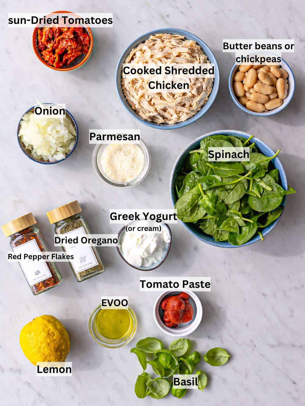 Ingredients arranged on marble surface with chicken, beans, yogurt, spinach, and sun-dried tomatoes.
