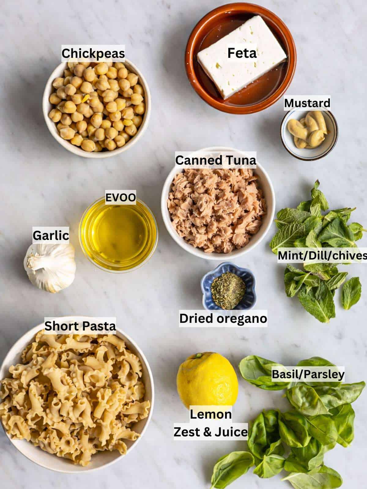 Ingredients for lemon tuna pasta salad arranged on marble surface in soft natural light.