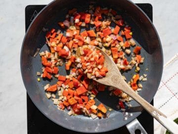 Step 1 Finely chopped red onions and bell peppers softening in a large skillet over a stovetop.