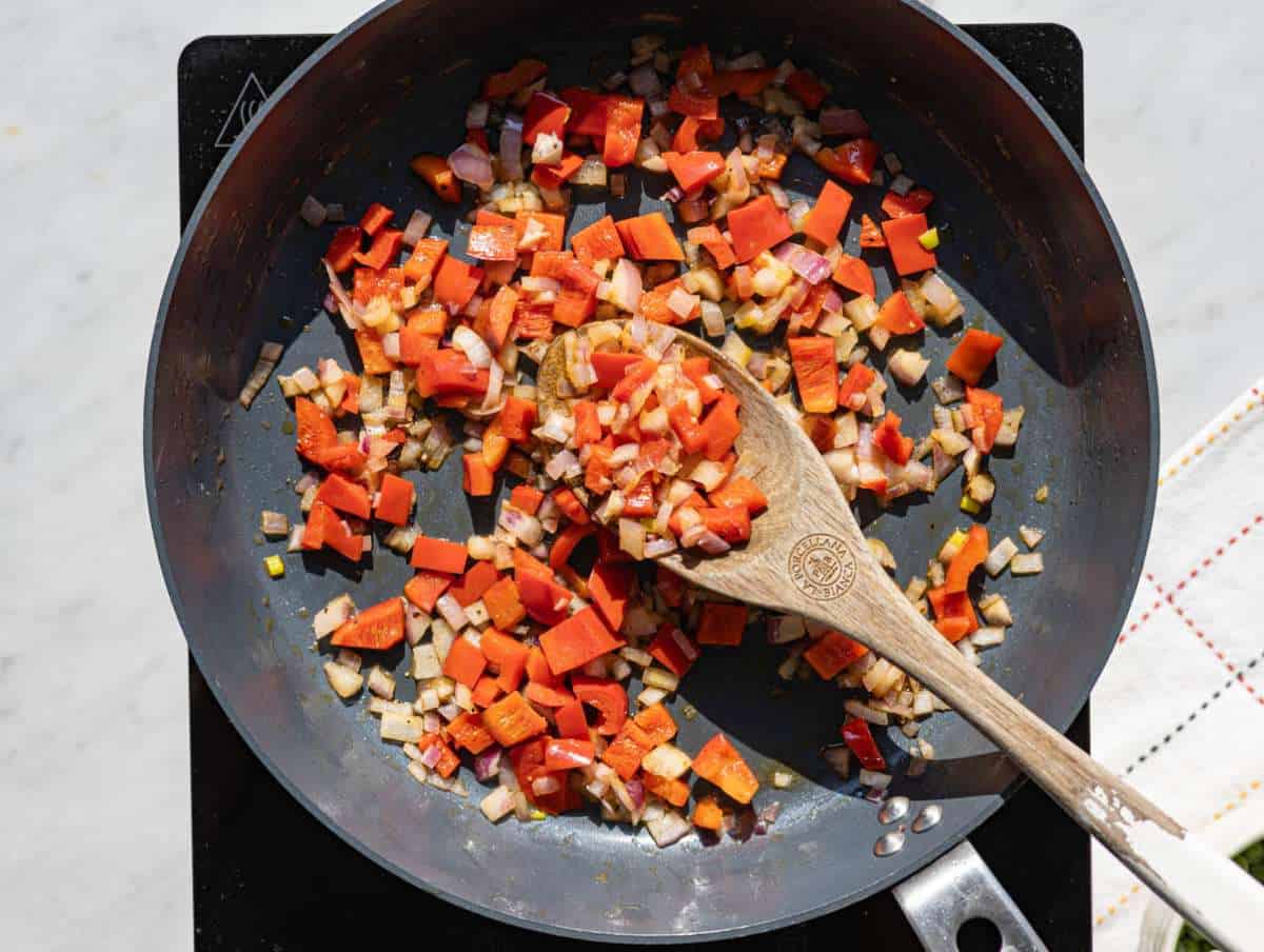 Step 1 Finely chopped red onions and bell peppers softening in a large skillet over a stovetop.