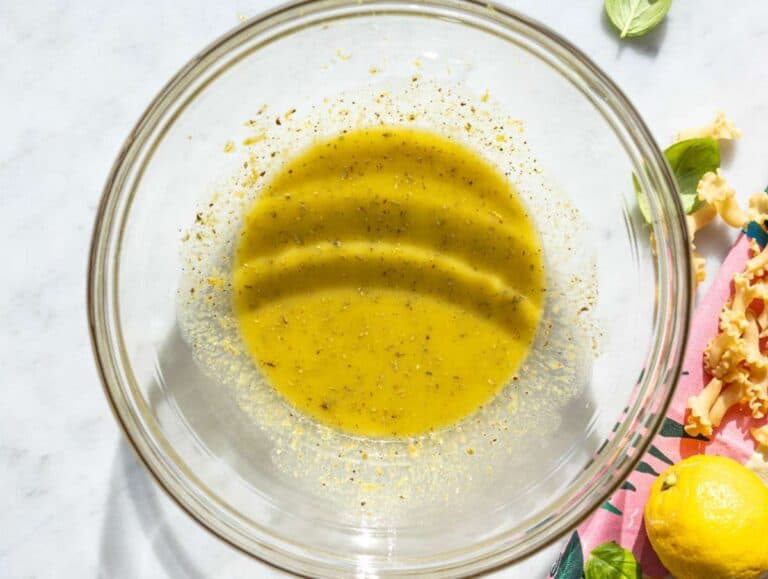 Step 1 Olive oil, lemon juice, and mustard being whisked in glass bowl.