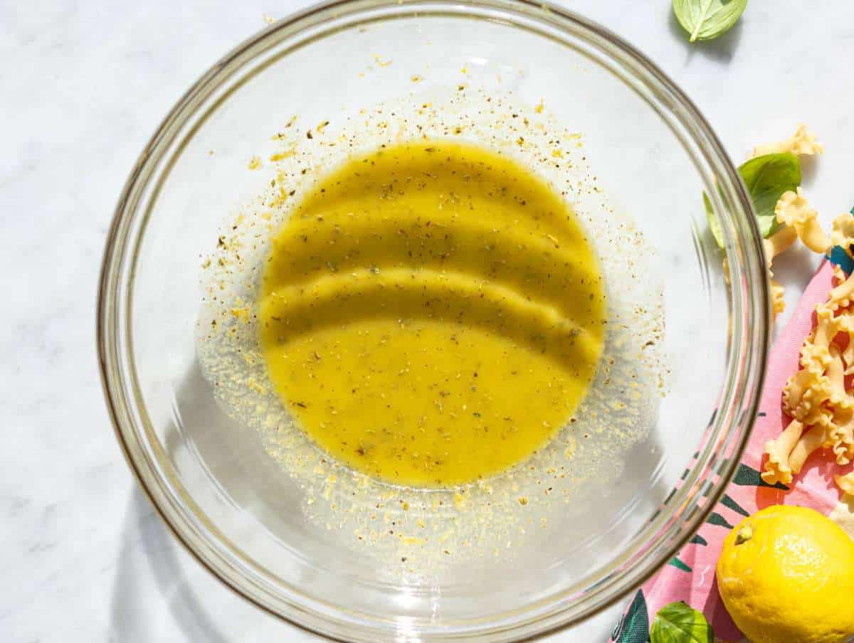 Step 1 Olive oil, lemon juice, and mustard being whisked in glass bowl.