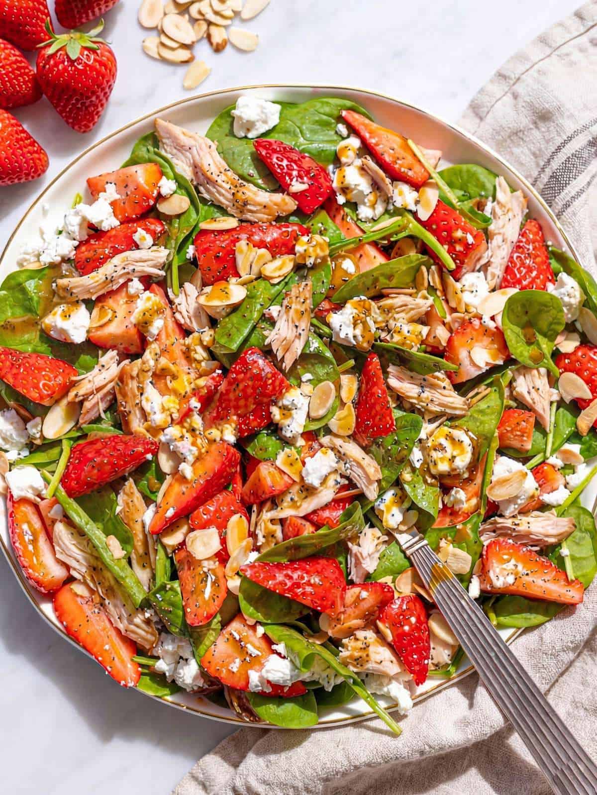 Strawberry spinach chicken salad in a large bowl with feta and almonds, natural light.