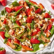 Strawberry spinach chicken salad served on marble table near window with soft natural light.