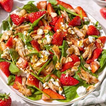 Strawberry spinach chicken salad served on marble table near window with soft natural light.