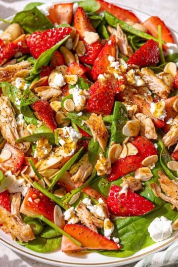 Strawberry spinach chicken salad served on marble table near window with soft natural light.