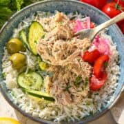 Close-up of creamy tuna rice bowl with cucumber, tomatoes, and herbs.