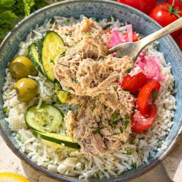 Close-up of creamy tuna rice bowl with cucumber, tomatoes, and herbs.