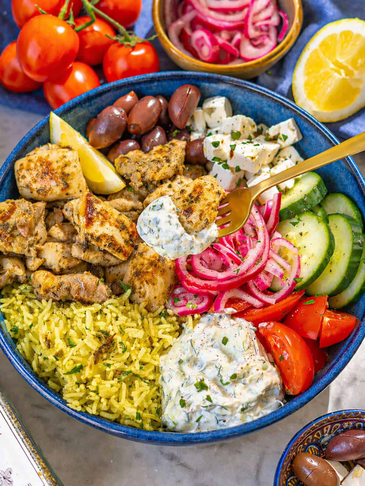Close up of juicy lemon garlic chicken over rice with fresh vegetables and feta.
