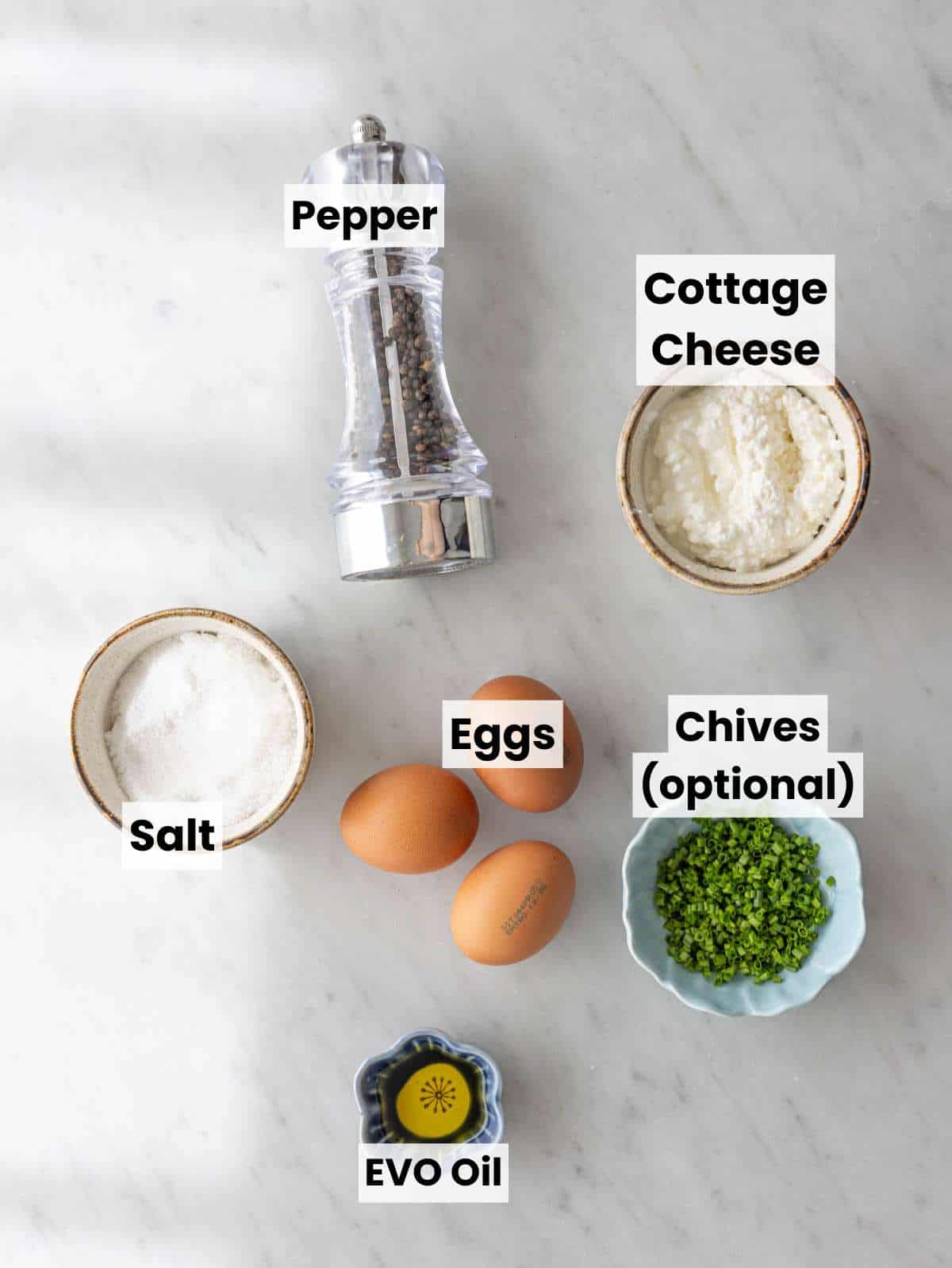 Eggs, cottage cheese, olive oil, salt, and pepper arranged on marble surface.