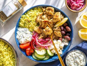 Step 3 Assembled Mediterranean chicken bowl with rice, chicken, and fresh toppings on marble surface.