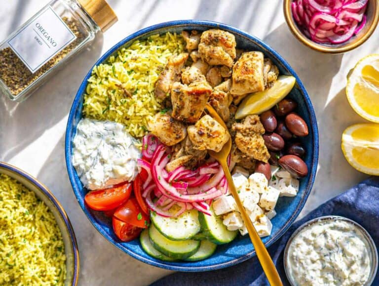 Step 3 Assembled Mediterranean chicken bowl with rice, chicken, and fresh toppings on marble surface.