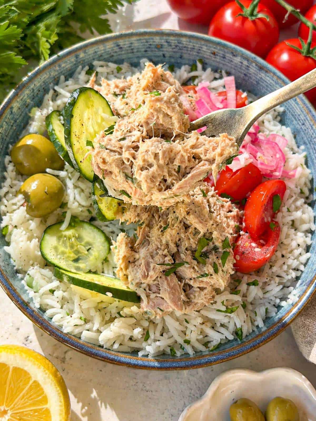 Tuna rice bowl with creamy tuna, cucumber, tomatoes, olives, and pickled onions on marble table.