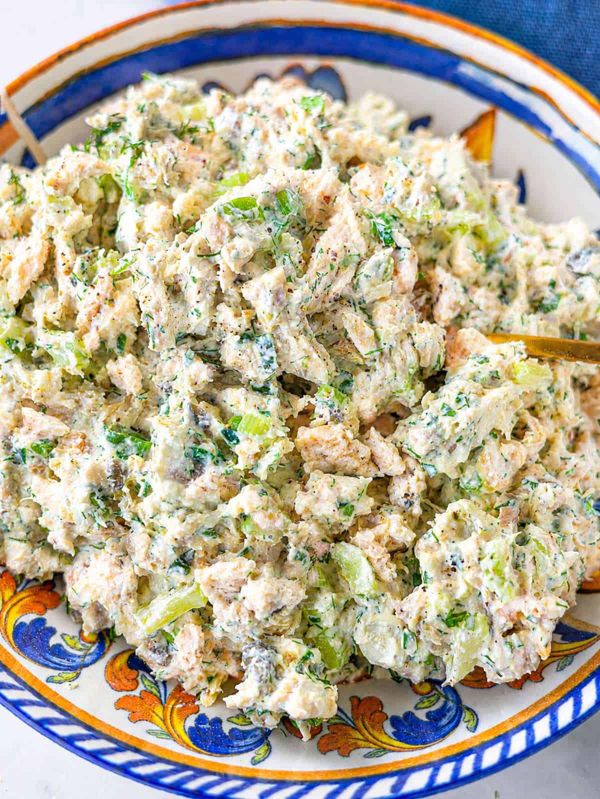 Close-up cottage cheese chicken salad with celery, herbs, and capers in ceramic bowl.