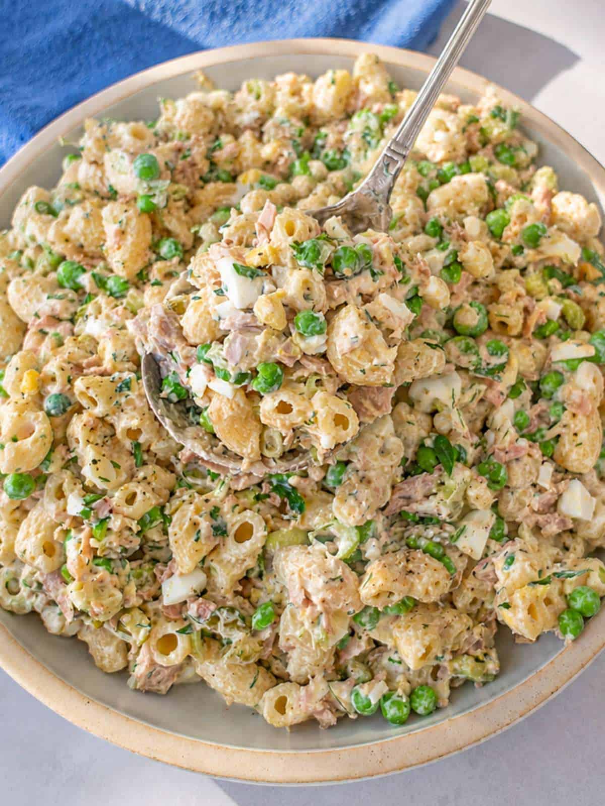 Creamy tuna macaroni salad with peas, eggs, and dill served in a white bowl.