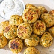 Golden Greek turkey meatballs with fresh herbs and tzatziki near bright kitchen window.