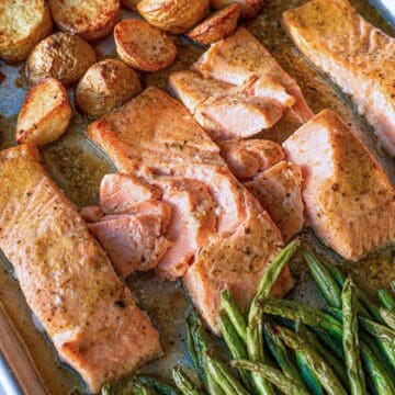 Golden roasted salmon with potatoes and green beans on a silver baking tray.