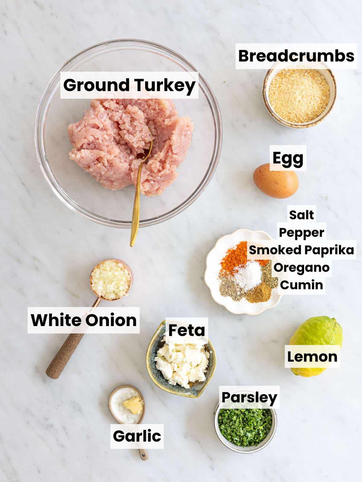 Ingredients for Greek turkey meatballs with feta, herbs, spices, and lemon on marble countertop.